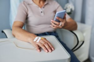 Close up of unrecognizable woman holding smartphone during IV drip treatment