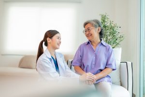 Asian female doctor taking care and talking mature female patient sitting on sofa in hospital. Healthcare concept.